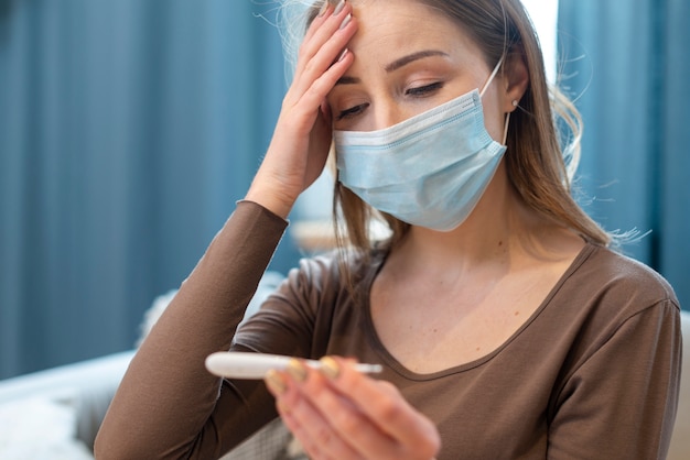 Giovane adulto che indossa una maschera di protezione che controlla il termometro