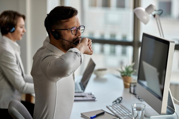 Giovane agente di call center che si sente esausto e sbadiglia mentre lavora in ufficio