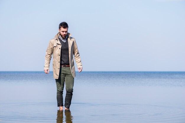 Giovane alla moda che cammina nell&#39;acqua di mare bassa contro cielo blu