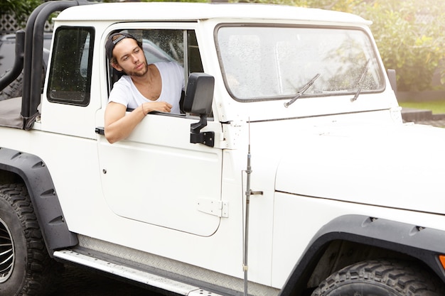 Giovane alla moda che guida il suo veicolo a quattro ruote motrici bianco