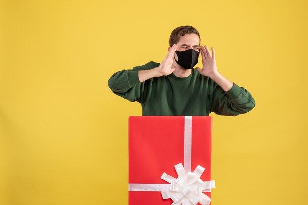 Giovane arrabbiato di vista frontale con la maschera che sta dietro il grande giftbox su colore giallo