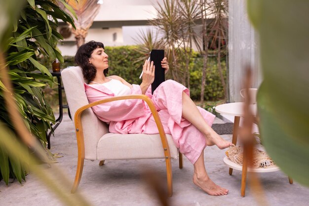 Giovane artista caucasica ragazza bruna in abiti rosa fa schizzi in tablet seduto su una sedia in cortile Concetto di hobby e piacere