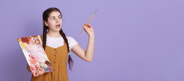 Giovane artista femminile con due trecce che tengono il pennello e la tavolozza in mani