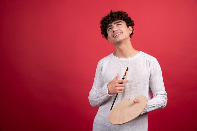 Giovane artista maschio con tavolozza e pennelli sorridenti.