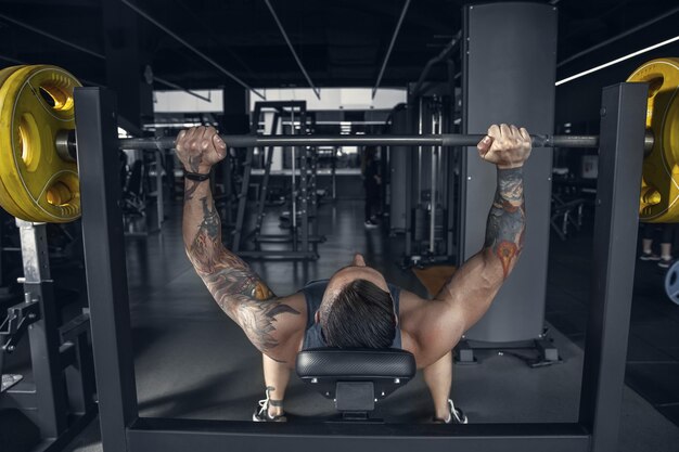 Giovane atleta caucasico muscolare che pratica pull-up in palestra con bilanciere.