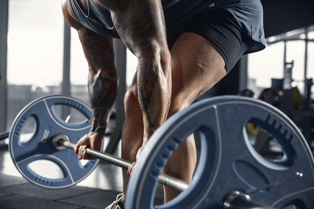 Giovane atleta caucasico muscolare che pratica pull-up in palestra con bilanciere.