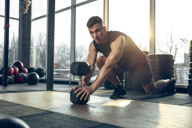 Giovane atleta caucasico muscolare che si allena in palestra, fa esercizi di forza, pratica, lavora sulla parte superiore del corpo con i pesi che rotolano.