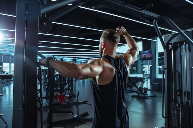 Giovane atleta caucasico muscolare che si allena in palestra, facendo esercizi di forza