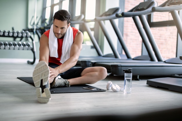 Giovane atleta che si allunga sul pavimento mentre ti alleni in palestra