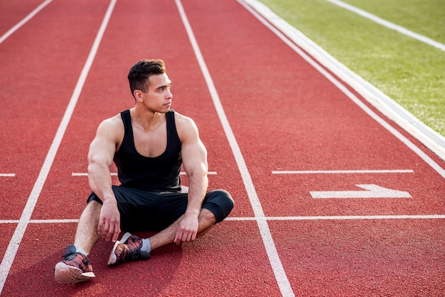 Giovane atleta maschio di forma fisica che si rilassa sulla pista di corsa rossa nello stadio