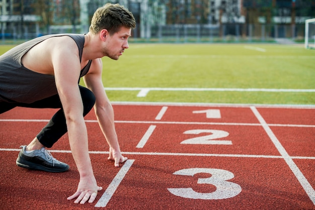 Giovane atleta maschio pronto a correre prendendo posizione sulla linea di partenza