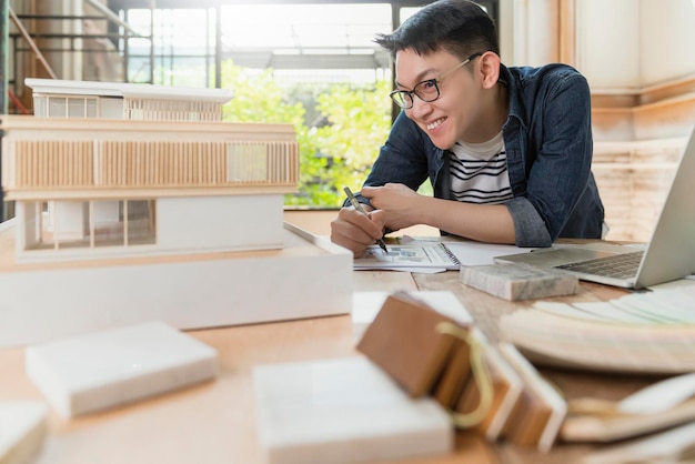 Giovane attraente asiatico occhiali maschio architetto sorriso fiducioso orgoglioso di presentare il nuovo progetto modello di casa felicità asiatica che lavora con lo studio del modello di massa del progetto di design della casa