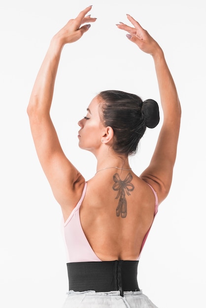 Giovane ballerina con fiocco e punta di piedi tatuaggio sulla schiena contro sfondo bianco