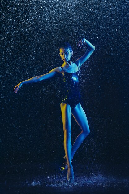 Giovane ballerina femminile che esegue sotto gocce d'acqua e spray. Modello caucasico ballando in luci al neon. Donna attraente. Balletto e concetto di coreografia contemporanea. Foto di arte creativa.