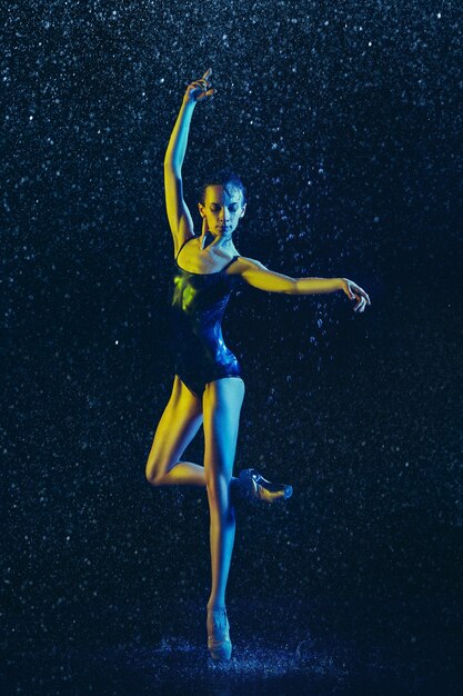 Giovane ballerina femminile che esegue sotto gocce d'acqua e spray. Modello caucasico ballando in luci al neon. Donna attraente. Balletto e concetto di coreografia contemporanea.