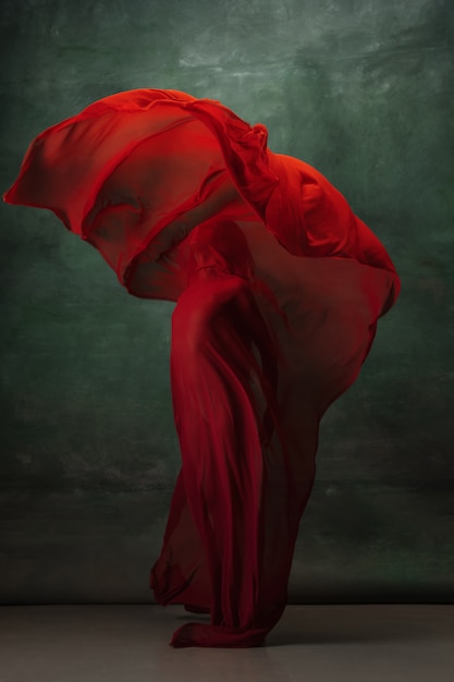Giovane ballerina tenera graziosa sullo spazio verde scuro dello studio con il panno rosso