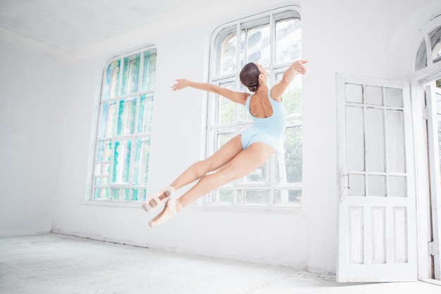 Giovane ballerino di balletto moderno che salta sulla parete bianca