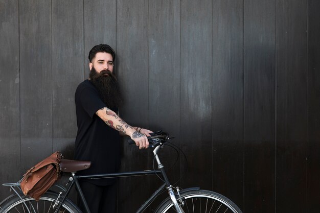 Giovane barbuto con la sua bicicletta davanti alla parete di legno nera