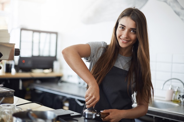 Giovane barista al lavoro che guarda l'obbiettivo sorridente, utilizzando un tamper per preparare un colpo di caffè espresso. Concetto di lavoro hipster.