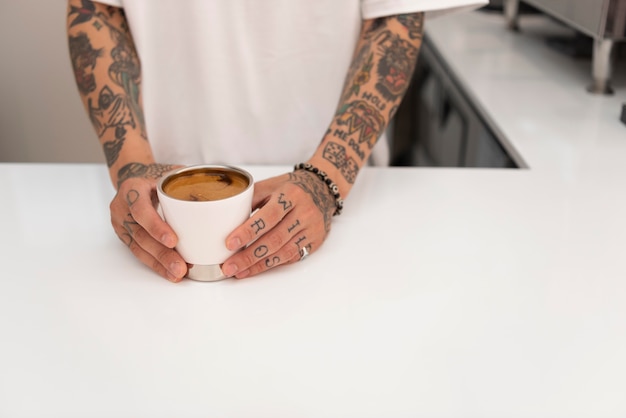 Giovane barista maschio con tatuaggi che tiene tazza di caffè appena fatto