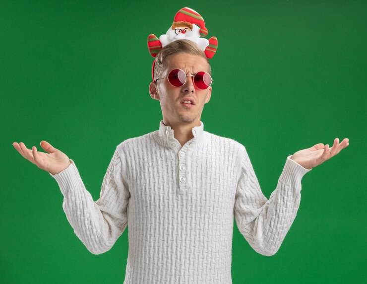 Foto gratuito giovane bel ragazzo senza tracce che indossa la fascia di babbo natale con gli occhiali che mostra le mani vuote isolate sulla parete verde