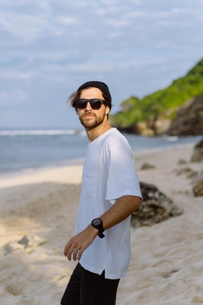 Giovane bell'uomo con un sorriso affascinante in occhiali da sole sulla spiaggia.