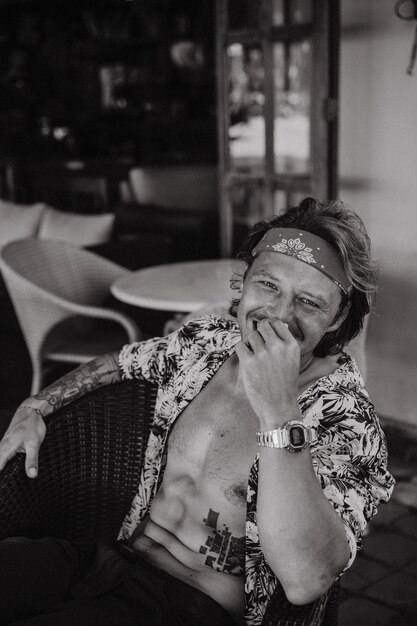 Giovane bell'uomo hippie con una bandana rossa, con un torso nudo in un caffè a Bali. Uomo felice che sorride