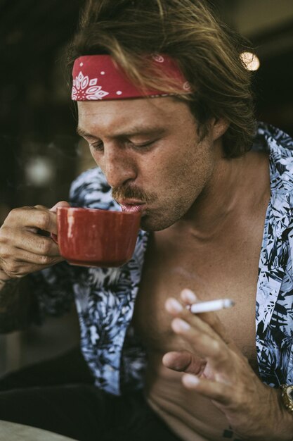 Giovane bell'uomo hippie con una bandana rossa, con un torso nudo in un caffè a Bali. Uomo felice che sorride