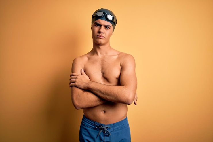 Foto gratuito giovane bell'uomo senza maglietta che indossa costume da bagno e cuffia da nuoto su sfondo giallo isolato espressione di disapprovazione scettica e nervosa sul viso con le braccia incrociate persona negativa