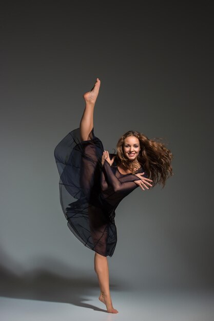 Giovane bella ballerina in abito nero in posa su uno sfondo di studio grigio scuro. Moderno, Contemporaneo, improvvisazione