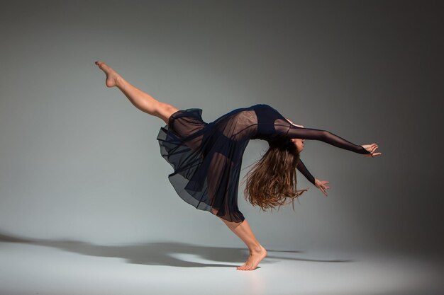 Giovane bella ballerina in abito nero in posa su uno sfondo di studio grigio scuro. Moderno, Contemporaneo, improvvisazione