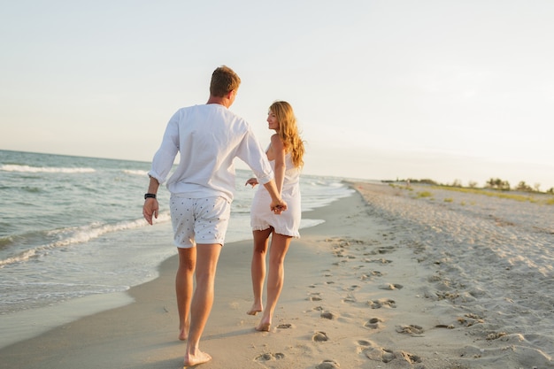 Giovane bella coppia cammina lungo la riva del mare al tramonto.