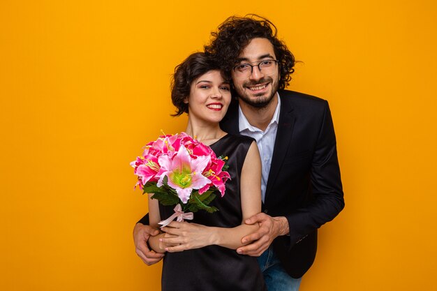 Giovane bella coppia felice uomo e donna con bouquet di fiori sorridenti allegramente abbracciati felici innamorati che celebrano san valentino