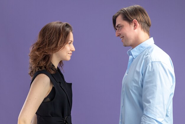 giovane bella coppia felice uomo e donna guardando l'altro sorridente per celebrare San Valentino in piedi su sfondo blu