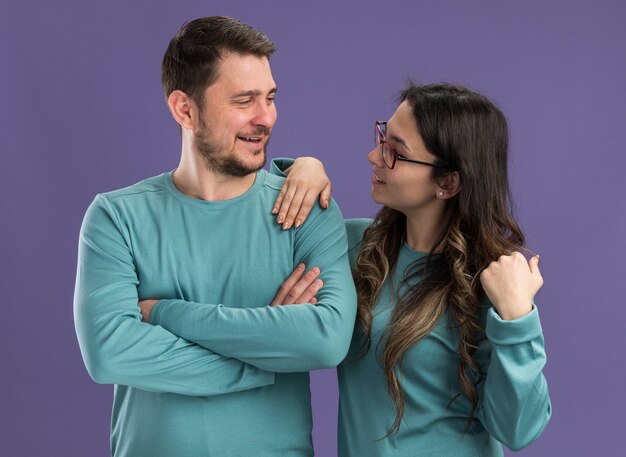 Giovane bella coppia in abiti casual blu uomo e donna che si guardano felici innamorati in piedi sul muro viola