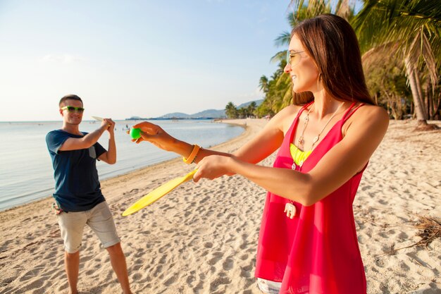 Giovane bella coppia innamorata giocando a ping pong sulla spiaggia tropicale, divertendosi, vacanze estive, attivo, sorridente, divertente, positivo