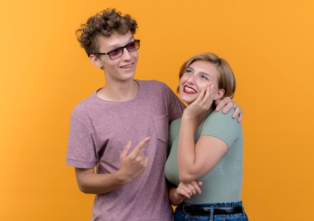 Giovane bella coppia uomo e donna che indossa abiti casual felice e positivo sorridente allegramente in piedi insieme sopra la parete arancione