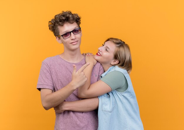 Giovane bella coppia uomo e donna che indossa abiti casual felici innamorati che stanno insieme sorridendo sopra la parete arancione