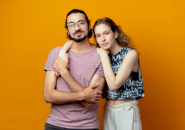 Giovane bella coppia uomo e donna felice in amore guardando la fotocamera in piedi su sfondo arancione