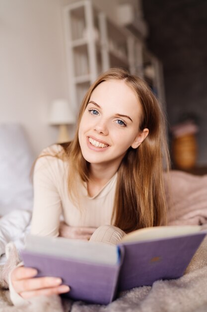 Giovane bella donna a letto a casa che si gode il libro preferito