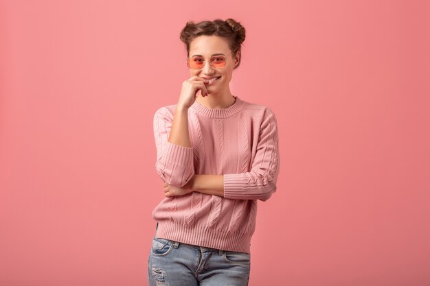 Giovane bella donna abbastanza sorridente in vestito alla moda primaverile che indossa un maglione rosa e occhiali da sole isolati su sfondo rosa studio