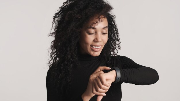 Giovane bella donna afro che sembra felice di rispondere ai messaggi utilizzando smartwatch per esso isolato su sfondo bianco