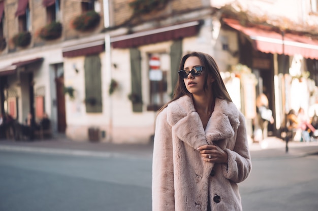 Giovane bella donna alla moda che cammina in cappotto rosa