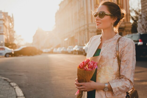 Giovane bella donna alla moda che cammina sulla strada della città sul tramonto