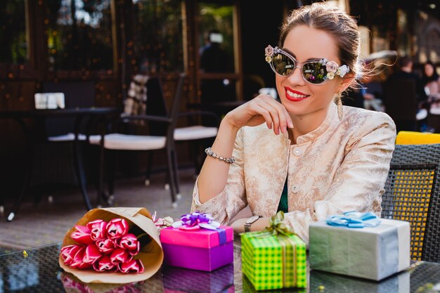 Giovane bella donna alla moda in occhiali da sole di modo che si siede al caffè