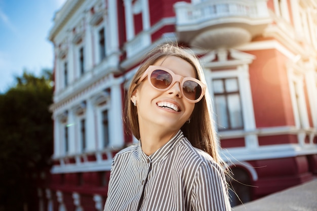 Giovane bella donna allegra in occhiali da sole a spasso per la città, sorridente.