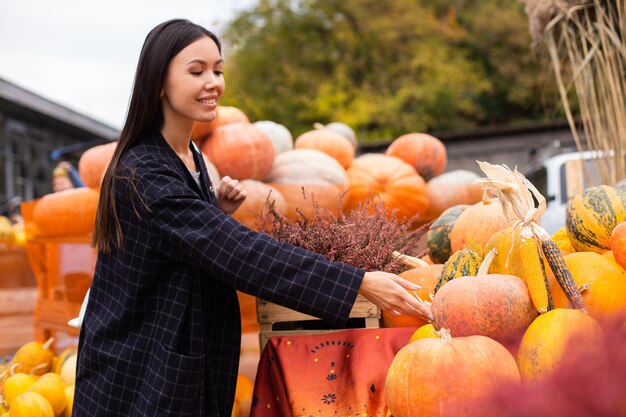 Giovane bella donna casual al negozio di fattoria felicemente alla ricerca di zucca per il giorno di Halloween all'aperto
