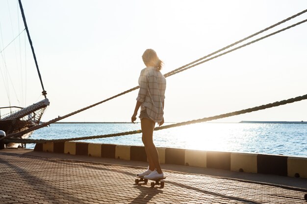 Giovane bella donna che cammina in riva al mare, skateboard