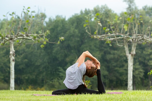 Giovane bella donna che fa esercizio di yoga nel parco verde. Stile di vita sano e concetto di fitness.