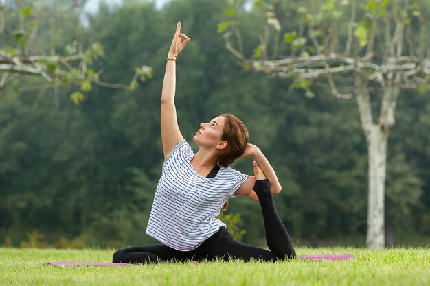 Giovane bella donna che fa esercizio di yoga nel parco verde. Stile di vita sano e concetto di fitness.